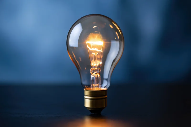 Glowing incandescent light bulb on dark reflective surface with blue background