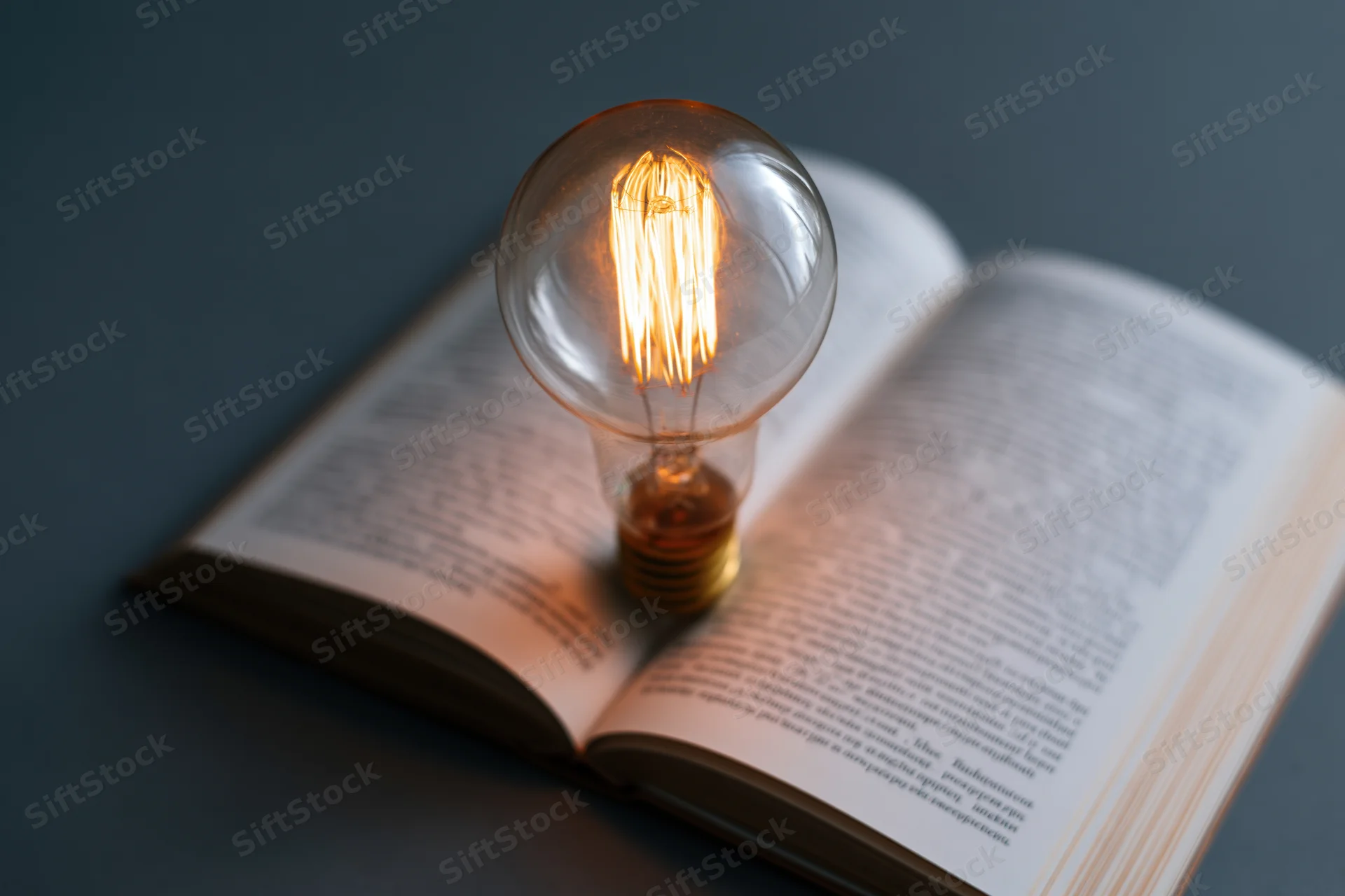 Glowing incandescent lightbulb resting on open book pages in dim lighting