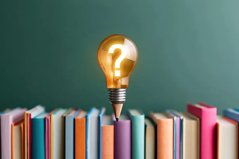 Glowing lightbulb with question mark above row of colorful books against green chalkboard background