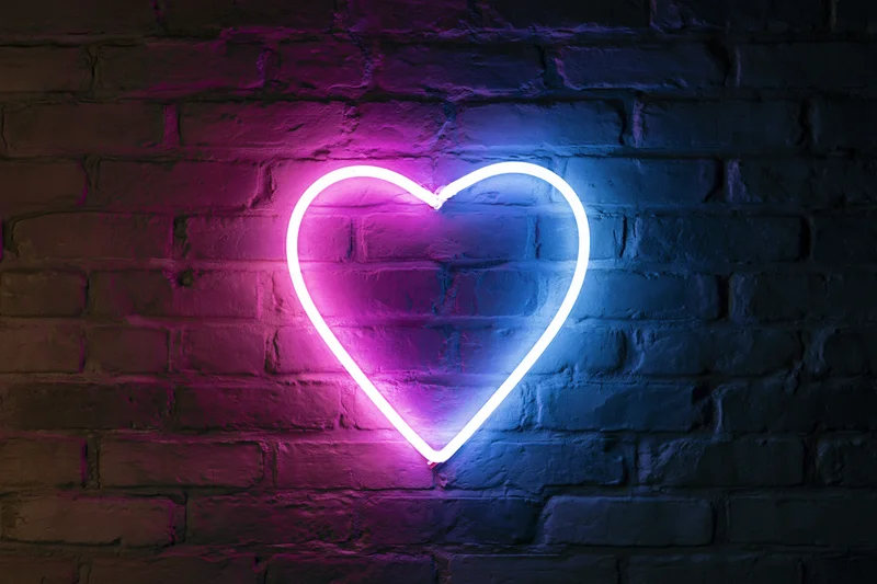Neon heart sign glowing on dark brick wall