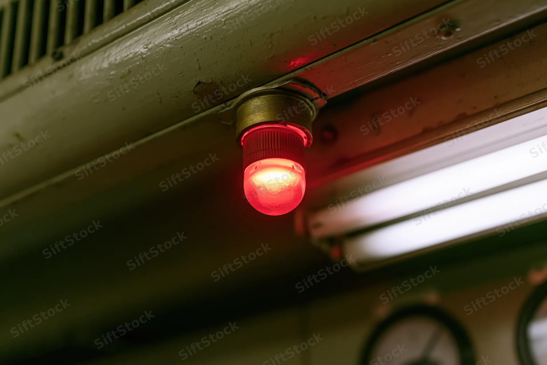 Red signal bulb glowing beneath metal industrial ceiling panel