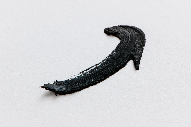 Black paint brushstroke forming a curved arrow pointing downward left on white background