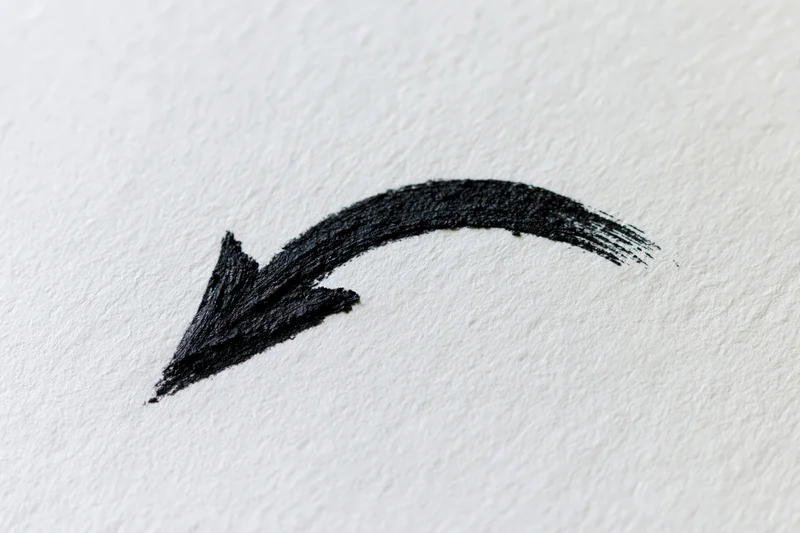 Hand-drawn curved arrow in black ink on white textured paper
