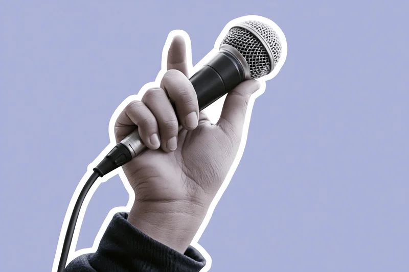 Hand gripping a wired microphone raised upward against a plain background