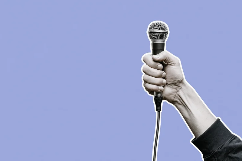 Hand gripping a wired microphone raised upward against a purple background