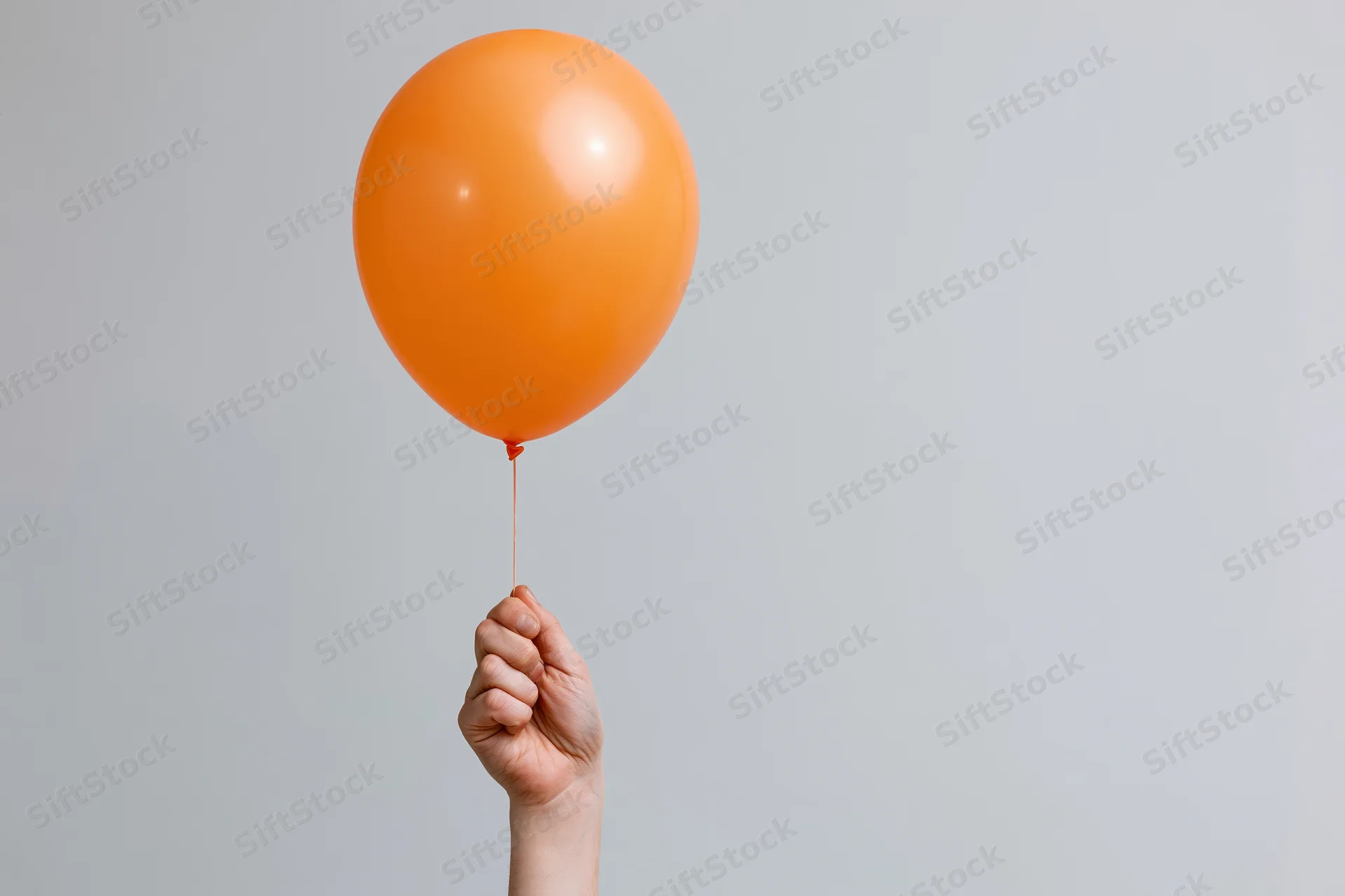 Hand holding orange balloon by string against plain background