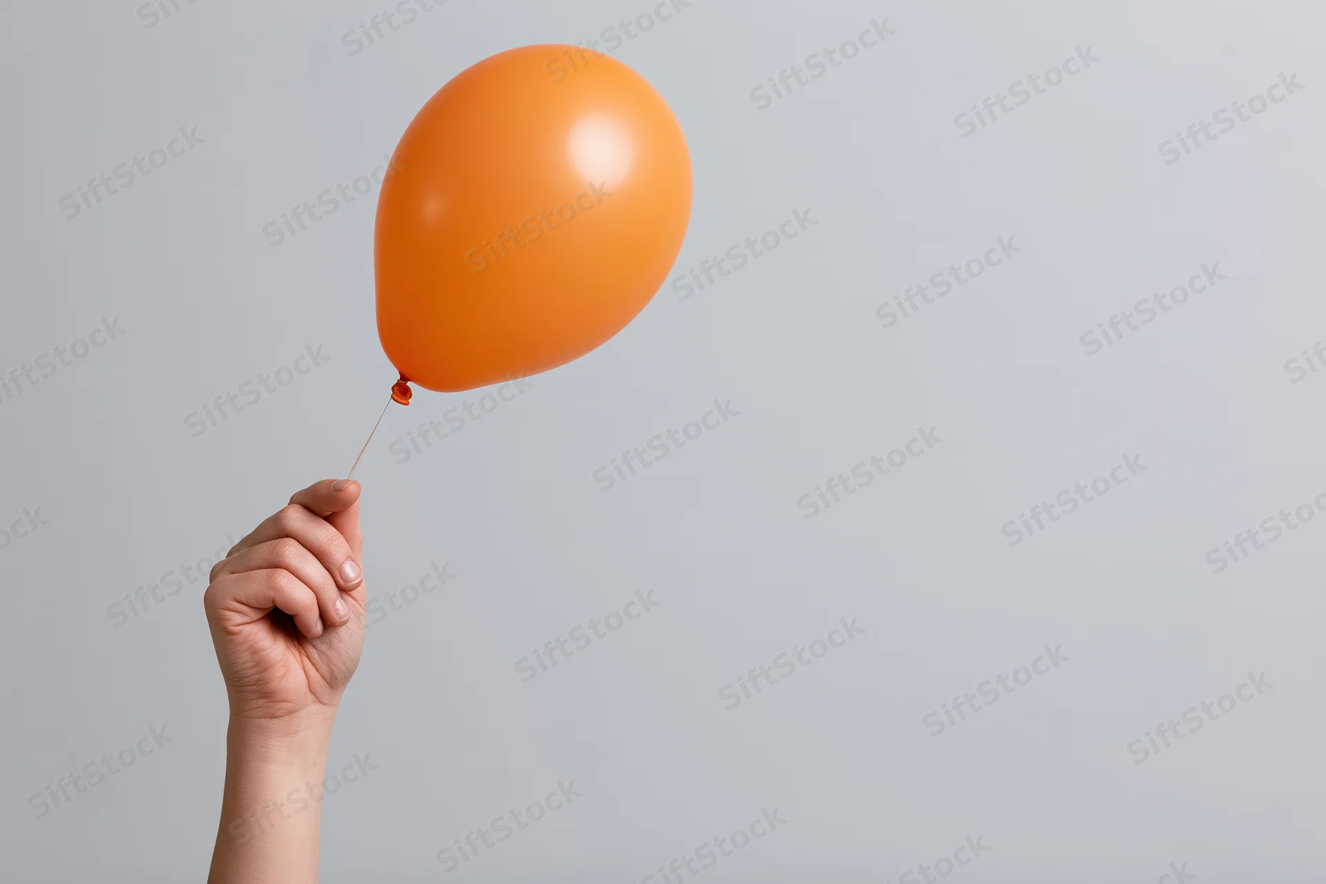 Hand holding an orange balloon by its string against a plain gray background