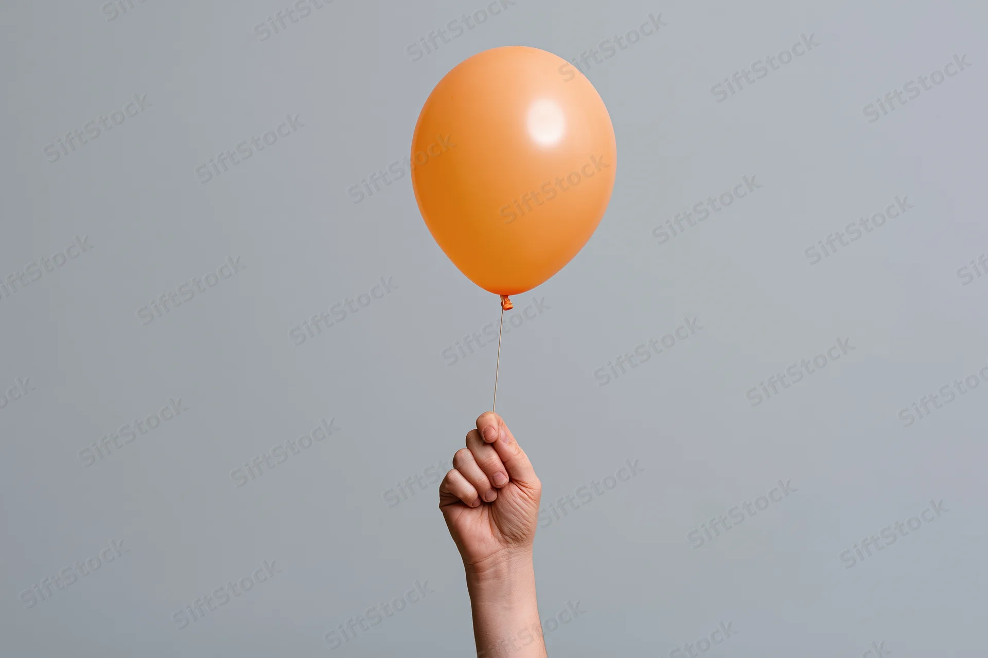 Hand holding orange balloon by string against gray background