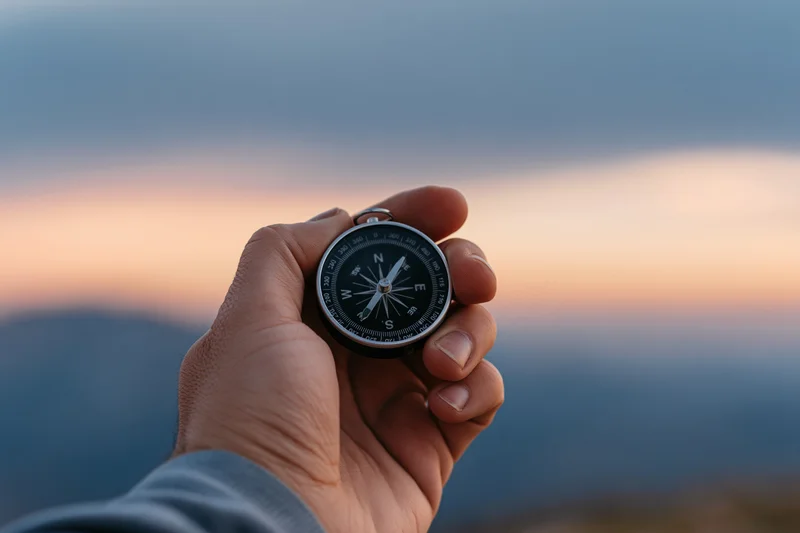 Hand holding compass against mountain sunset sky