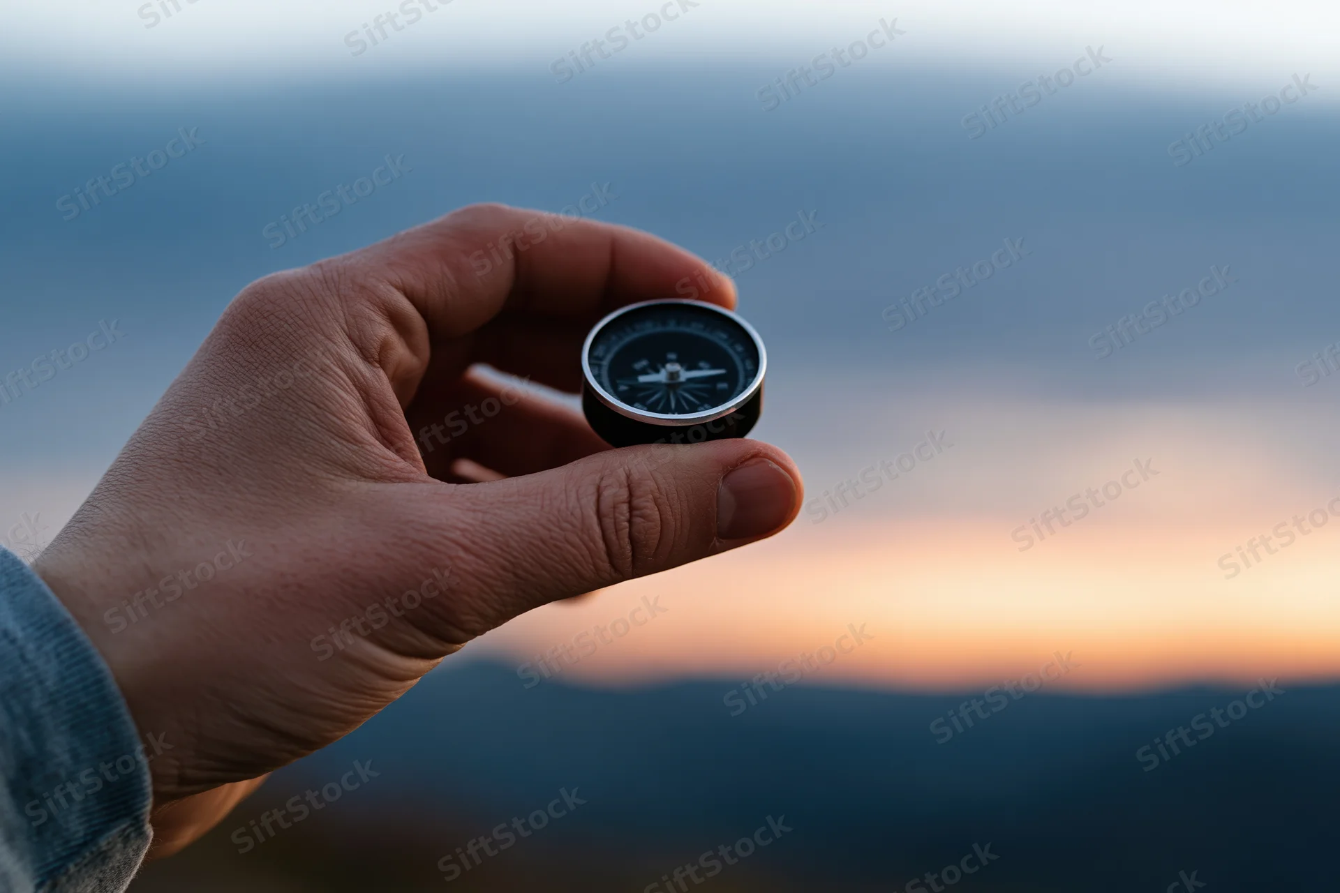 Hand holding a compass against a mountain sunset backdrop