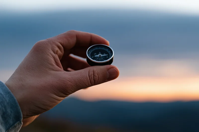 Hand holding a compass against a mountain sunset backdrop