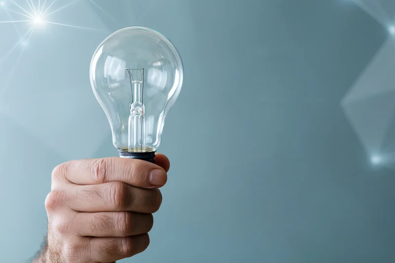 Hand holding a clear glass incandescent light bulb upright