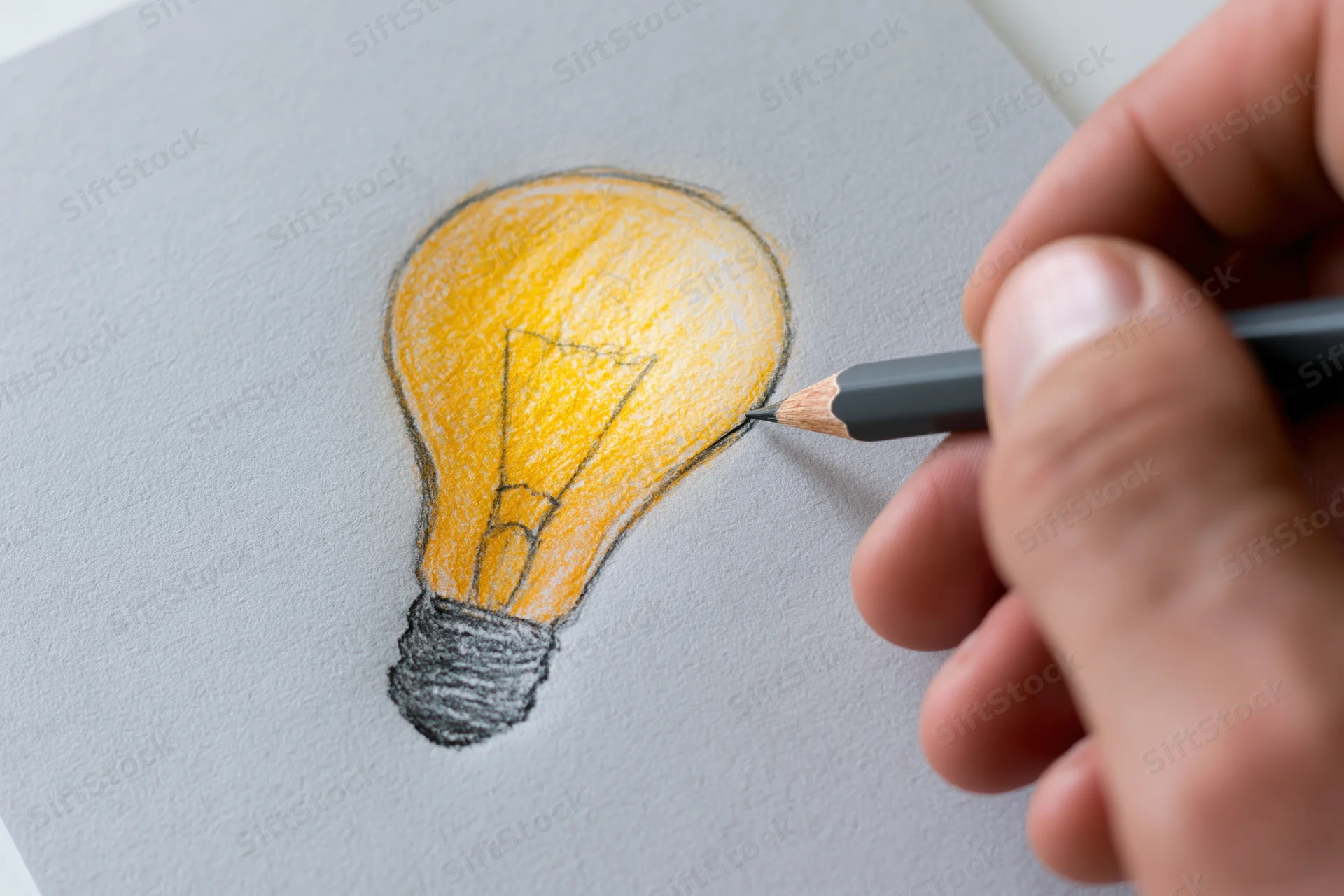 Hand drawing a glowing lightbulb on paper with a pencil