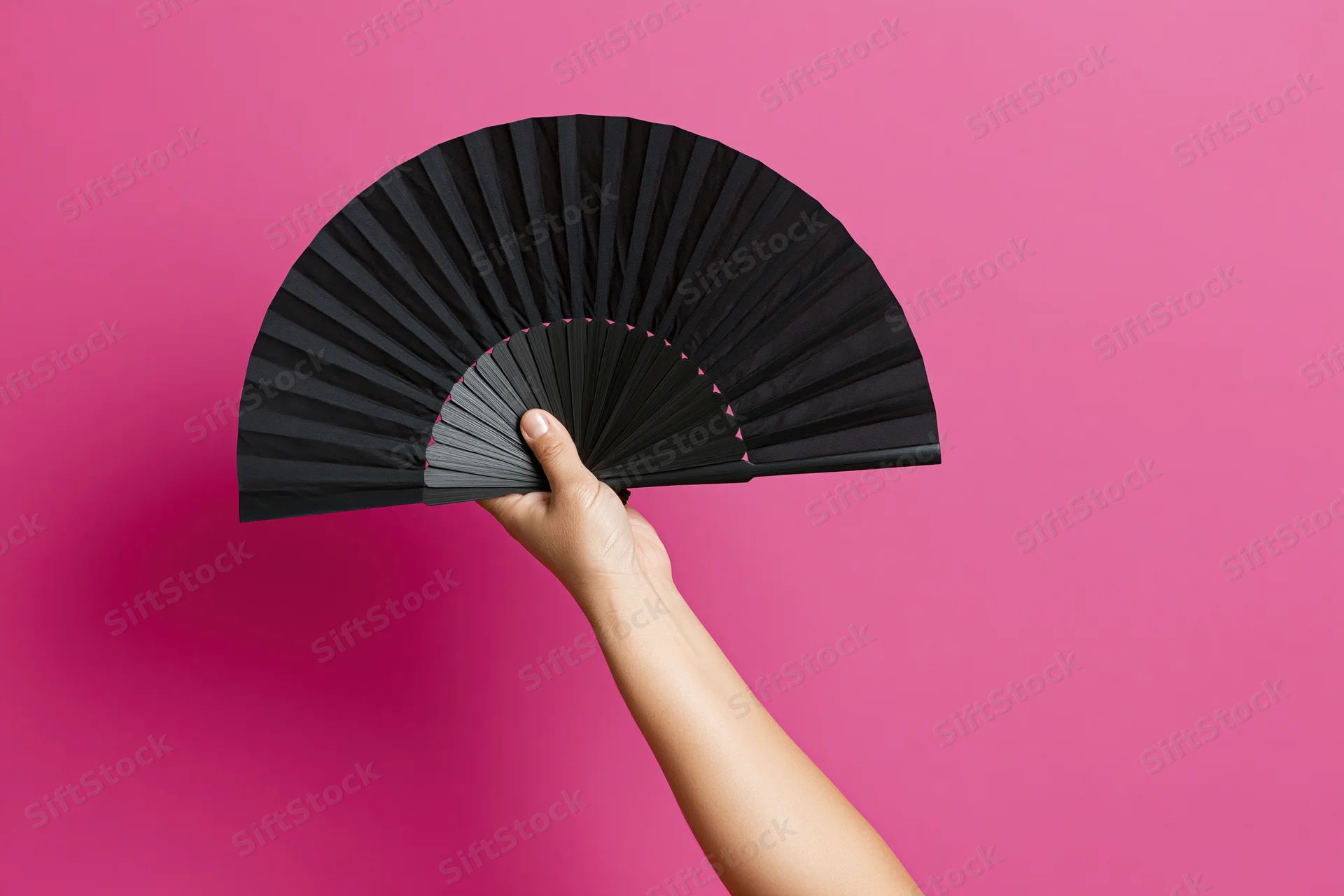 Hand holding open black folding fan raised upward against pink background
