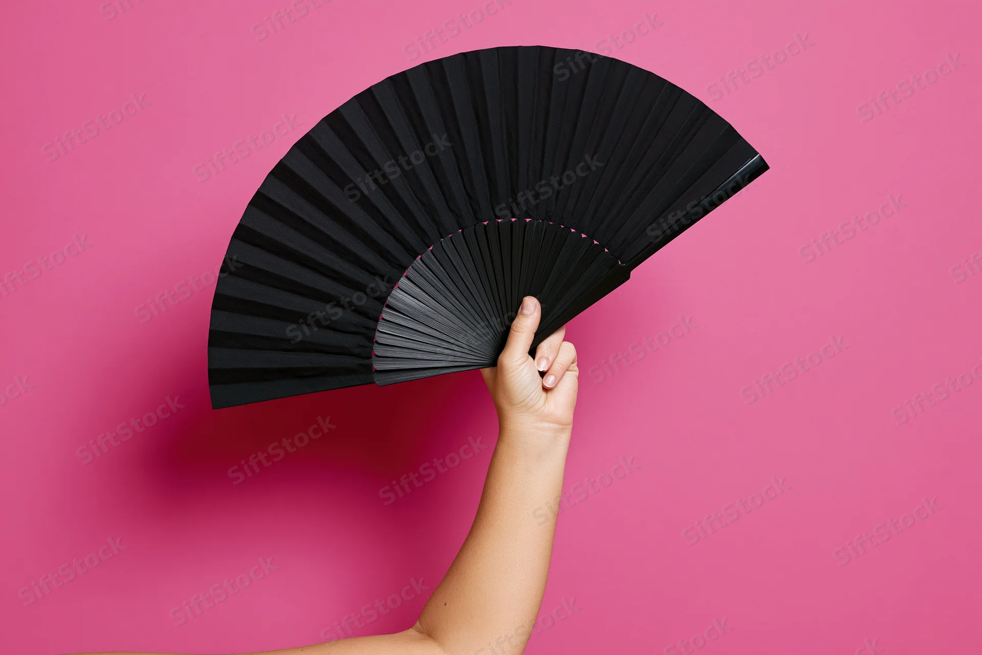 Hand holding open black folding fan against pink background