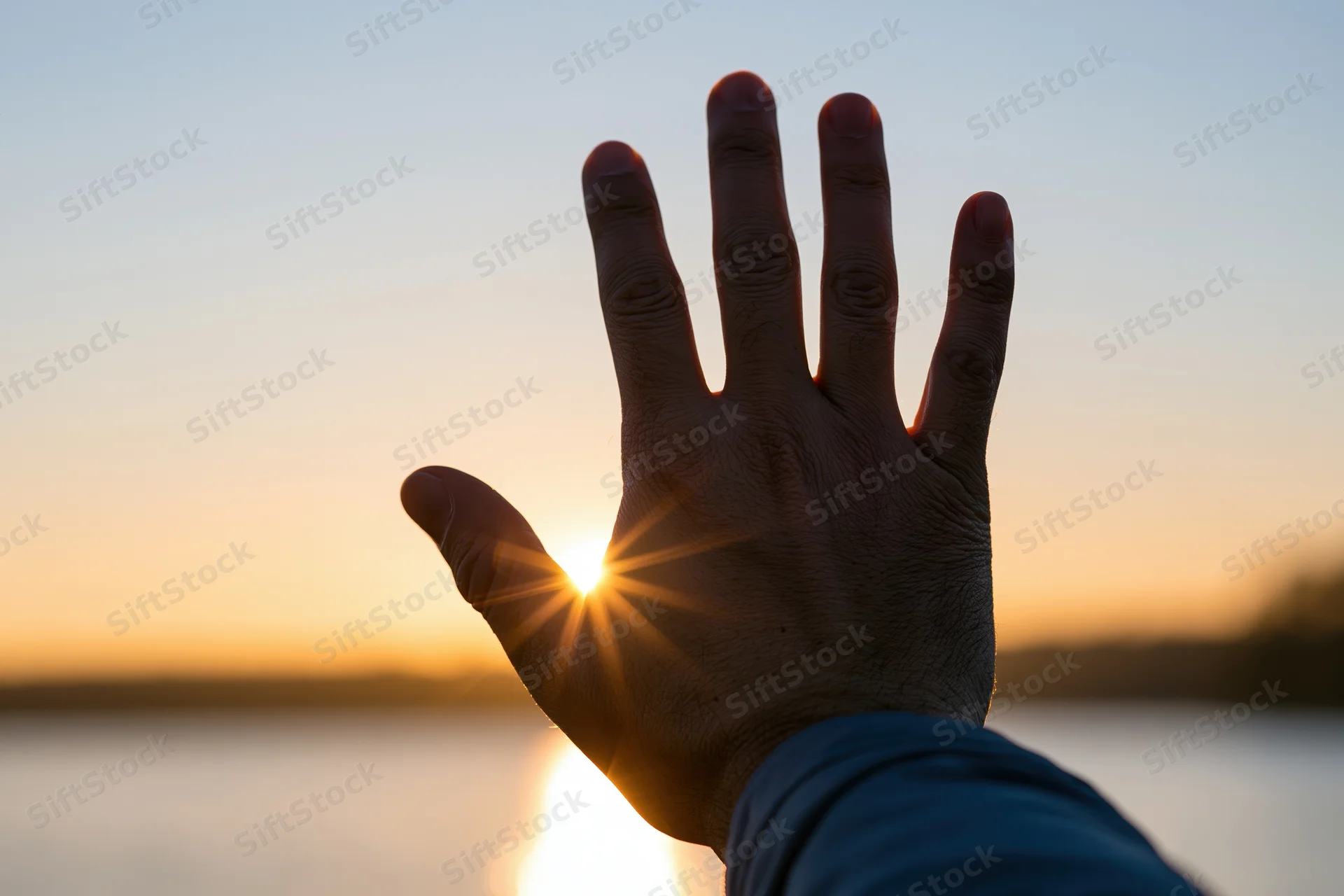 Hand raised palm up silhouetted against sunset over water