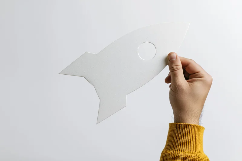 Hand holding white paper rocket cutout against plain background