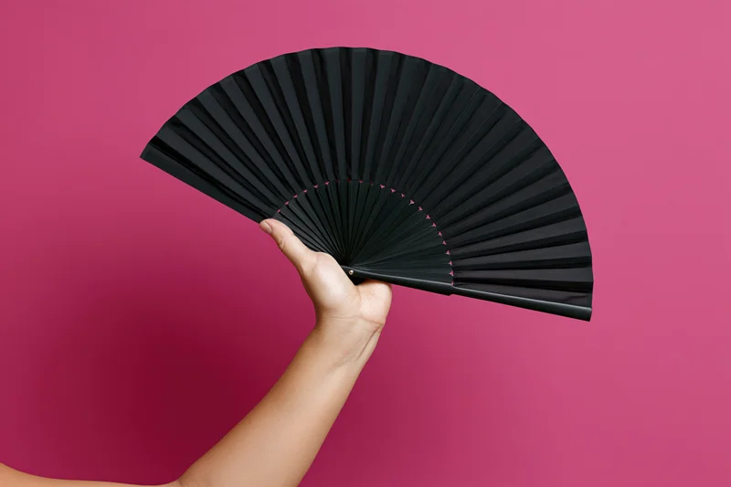 Hand holding open black folding fan against pink background