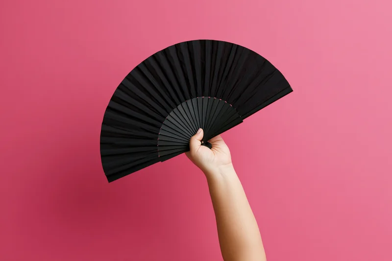 Hand holding open black folding fan against pink background