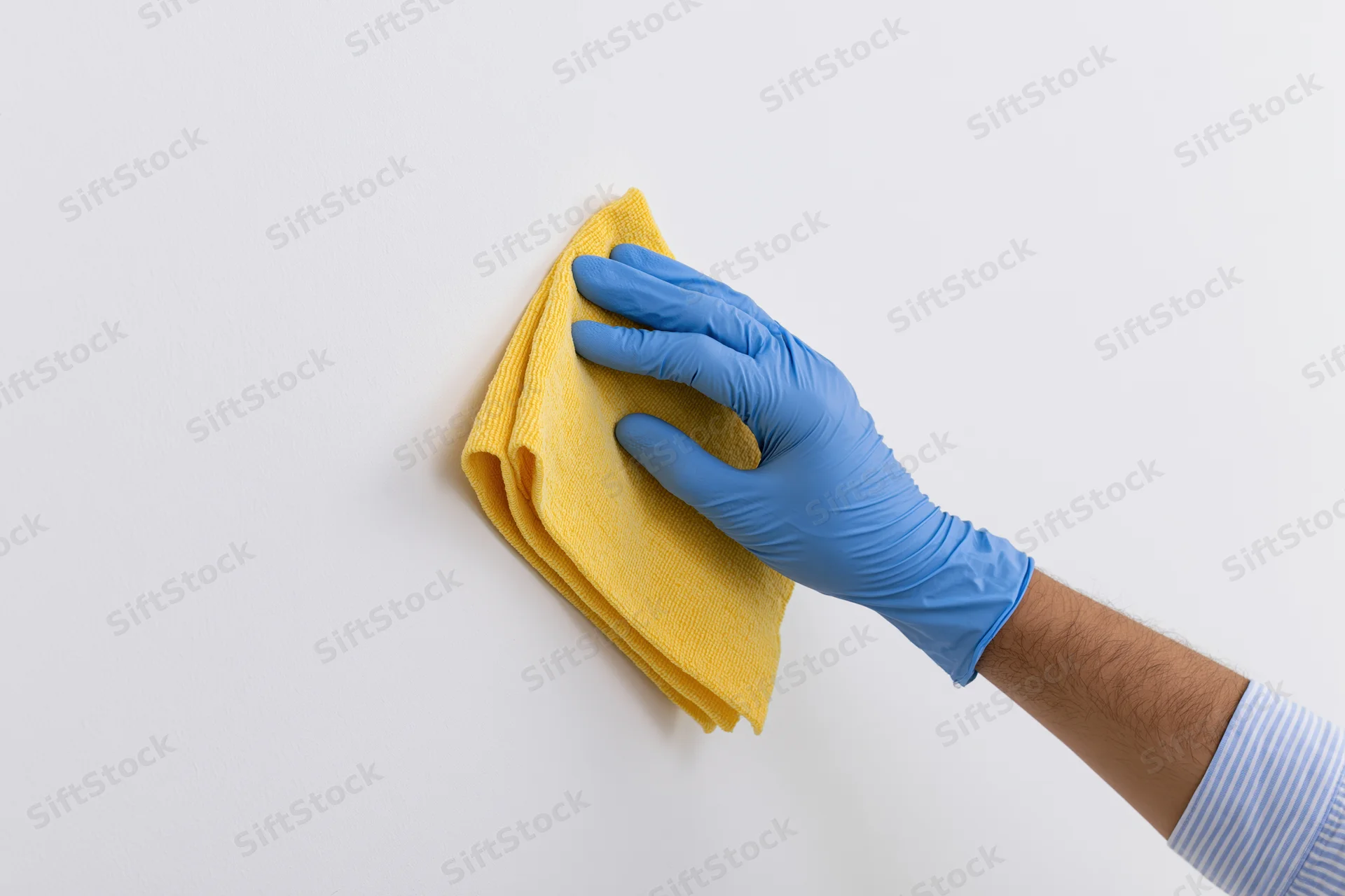 Hand in blue latex glove wiping white surface with yellow cloth
