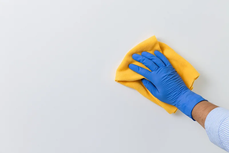 Hand in blue latex glove wiping white surface with yellow cloth