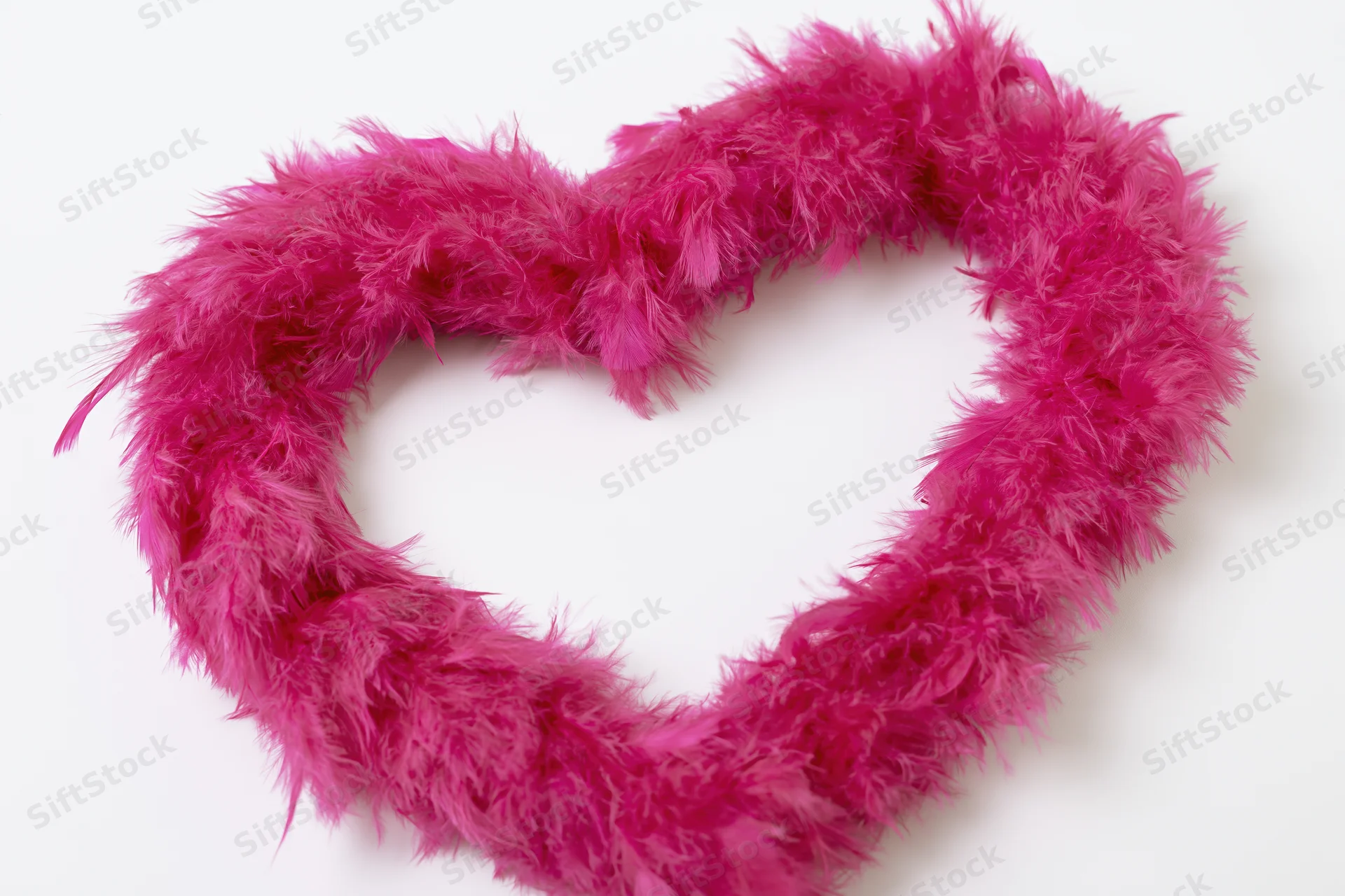 Heart-shaped frame made from hot pink feather boa on white background