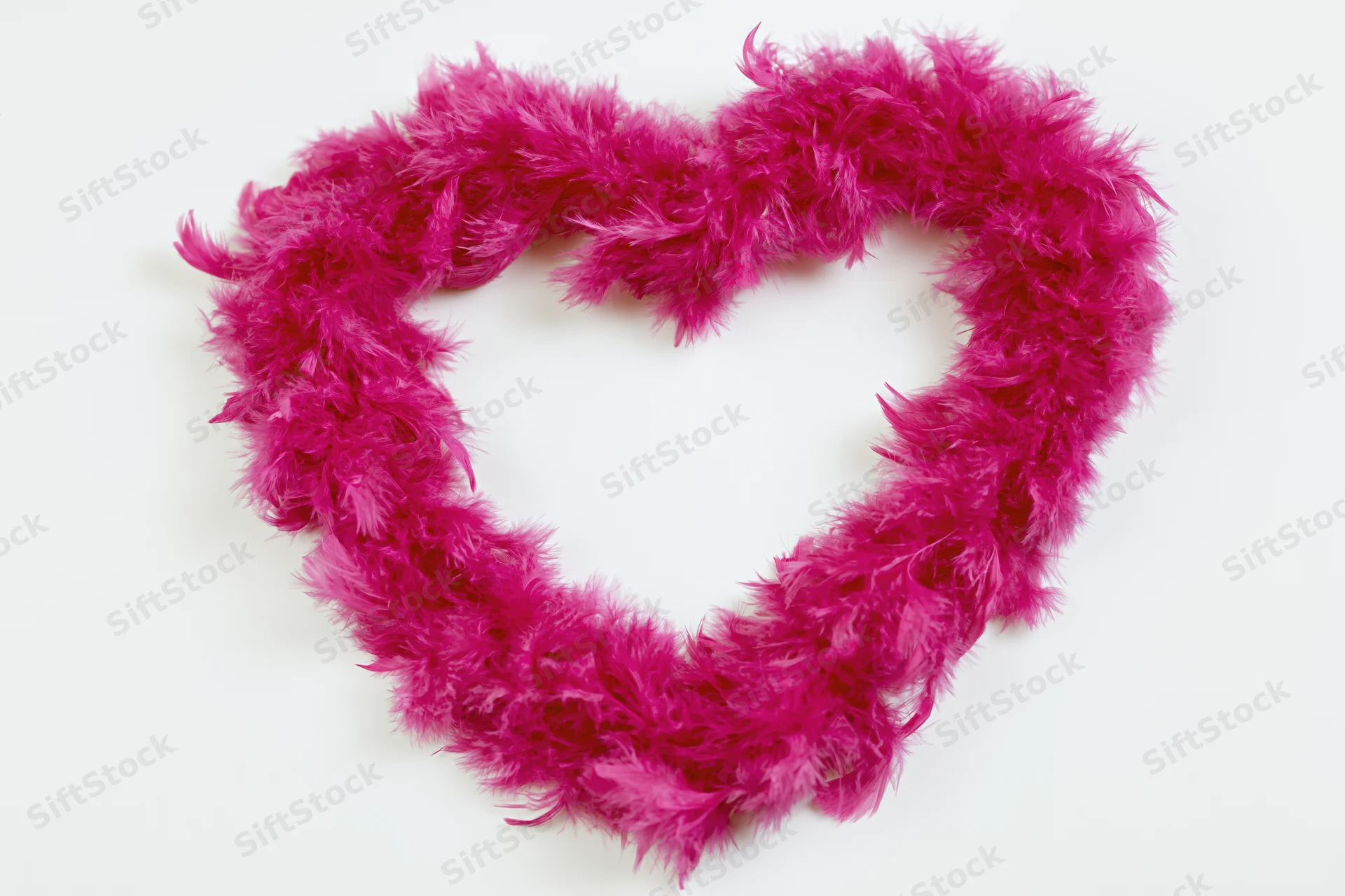 Heart-shaped frame made from hot pink feather boa on white background