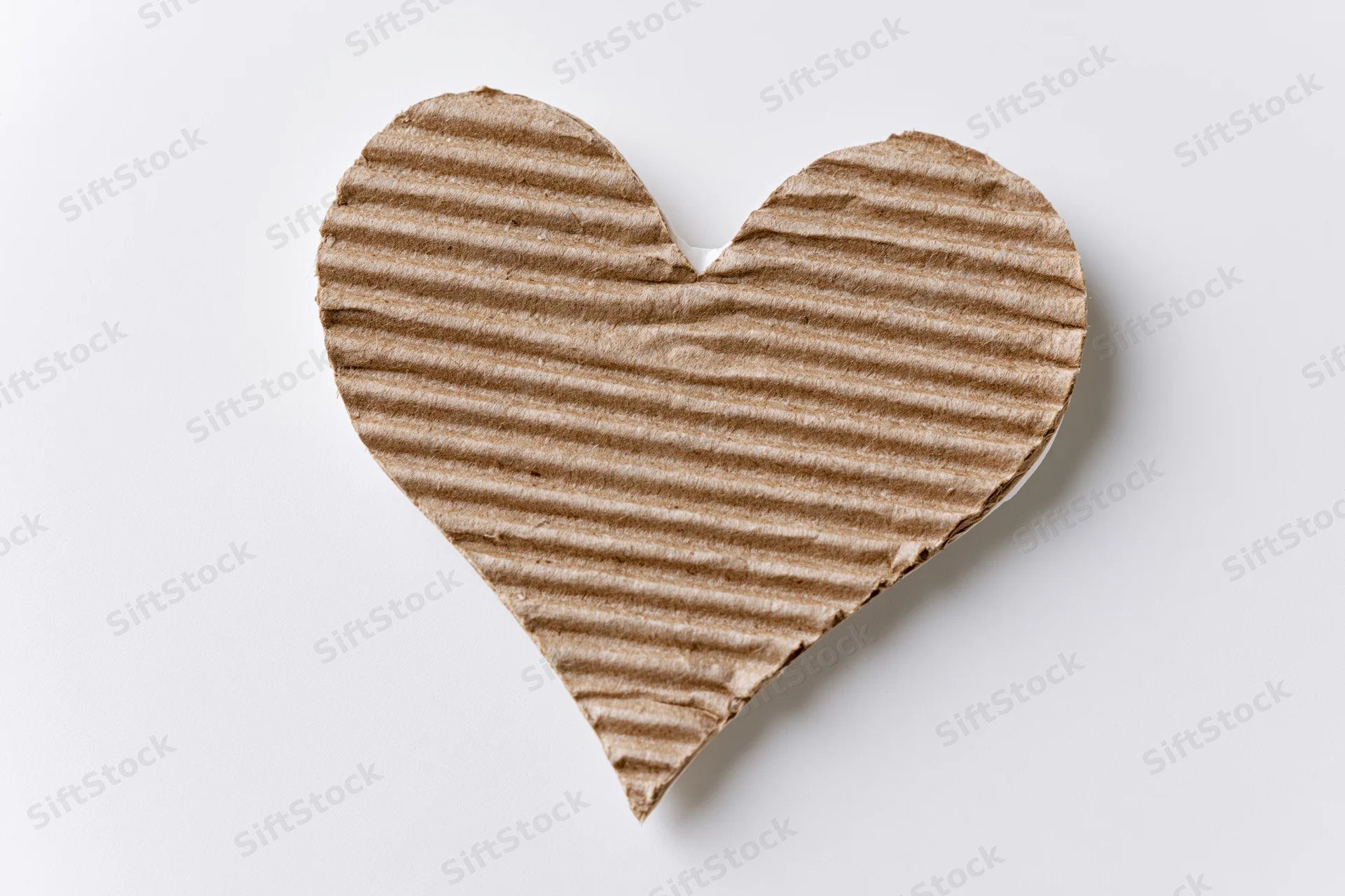 Heart-shaped corrugated kraft cardboard cutout lying flat on white background