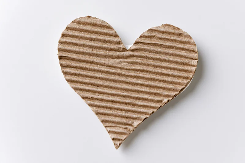 Heart-shaped corrugated kraft cardboard cutout lying flat on white background