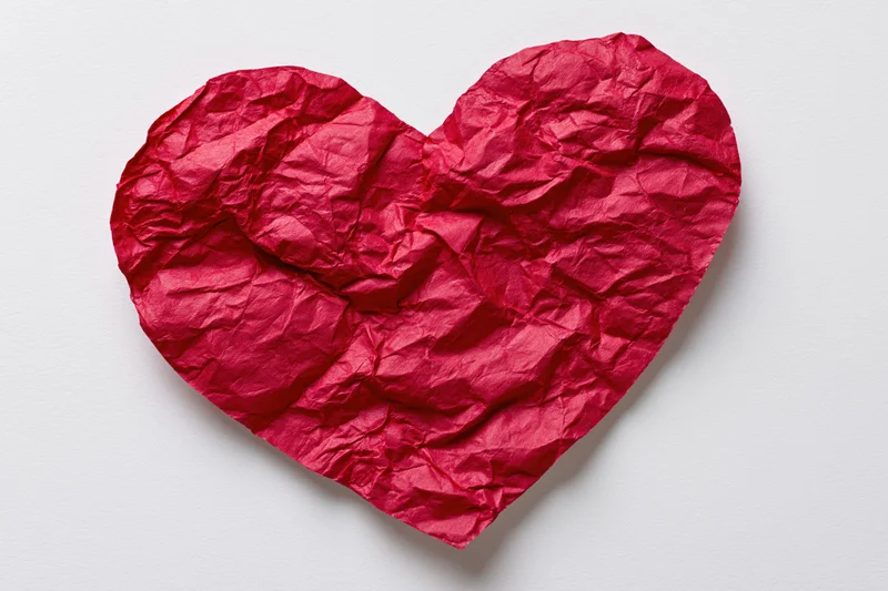 Crumpled red paper heart lying flat on white surface