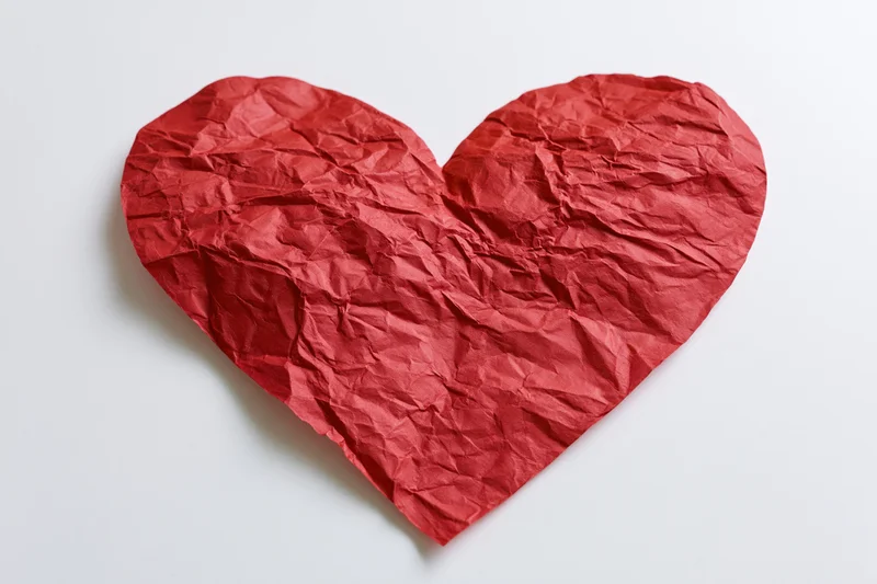 Crumpled red paper heart lying flat on white surface