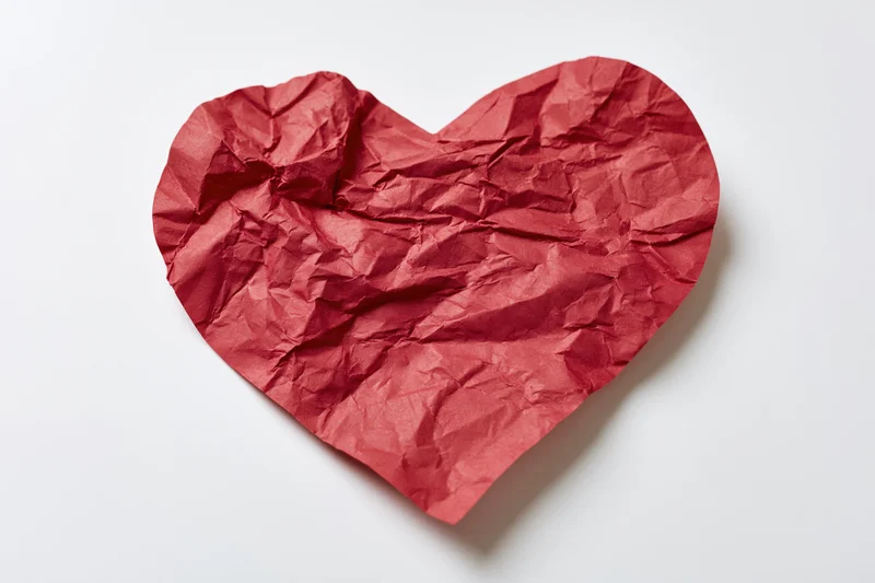 Crumpled red paper heart lying flat on white surface
