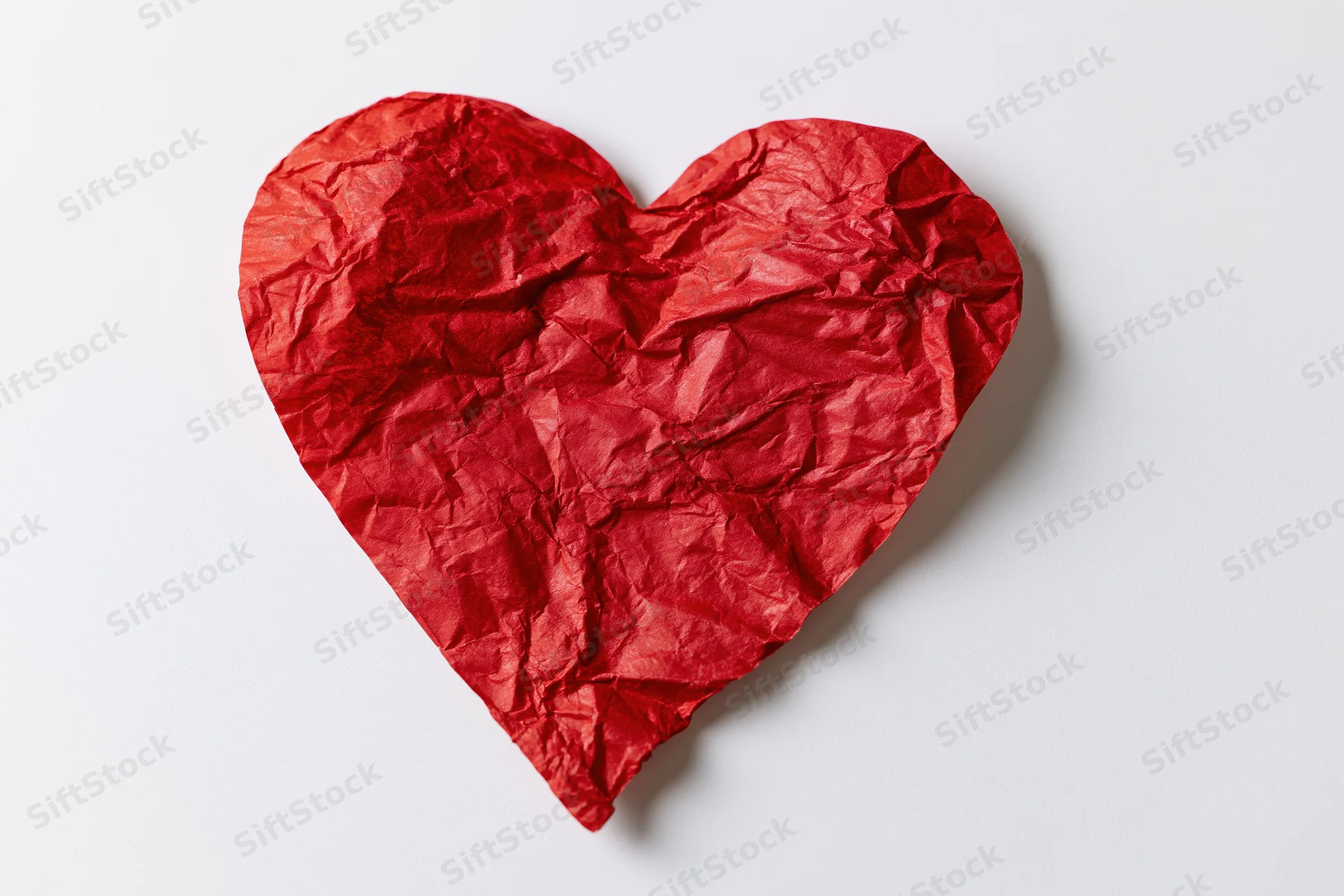 Crumpled red paper heart lying flat on white surface