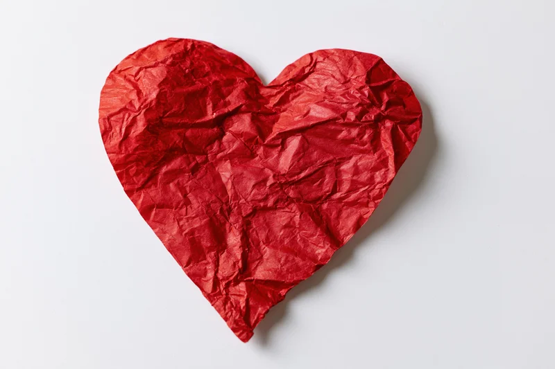 Crumpled red paper heart lying flat on white surface