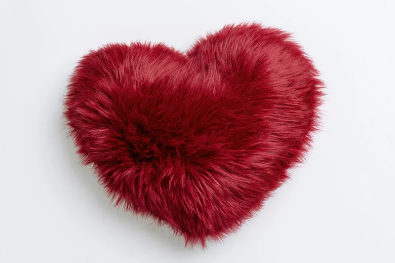 Red furry heart-shaped plush pillow on white background