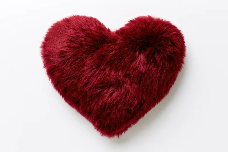 Red furry heart-shaped plush pillow on white background