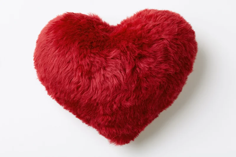 Red heart-shaped plush pillow with short dense fur on white background
