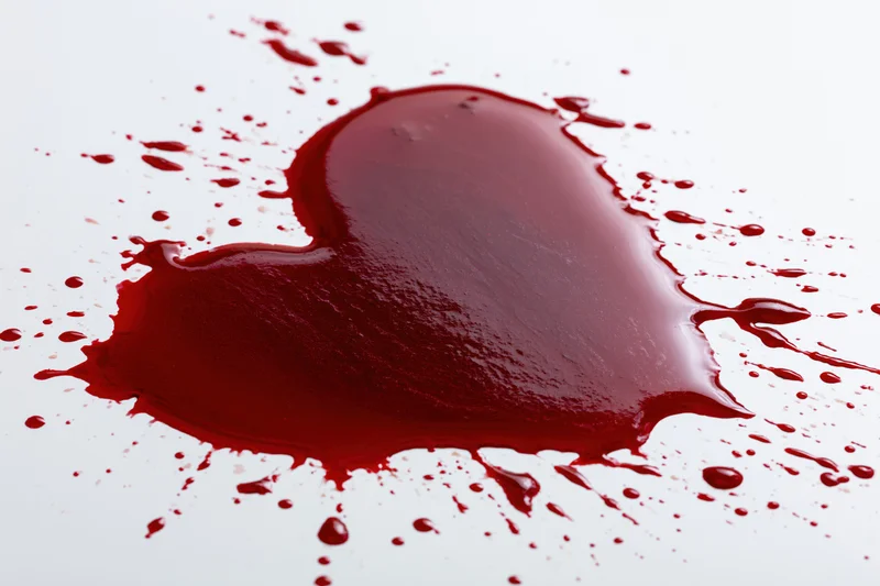 Heart-shaped pool of red liquid with splatters on white surface