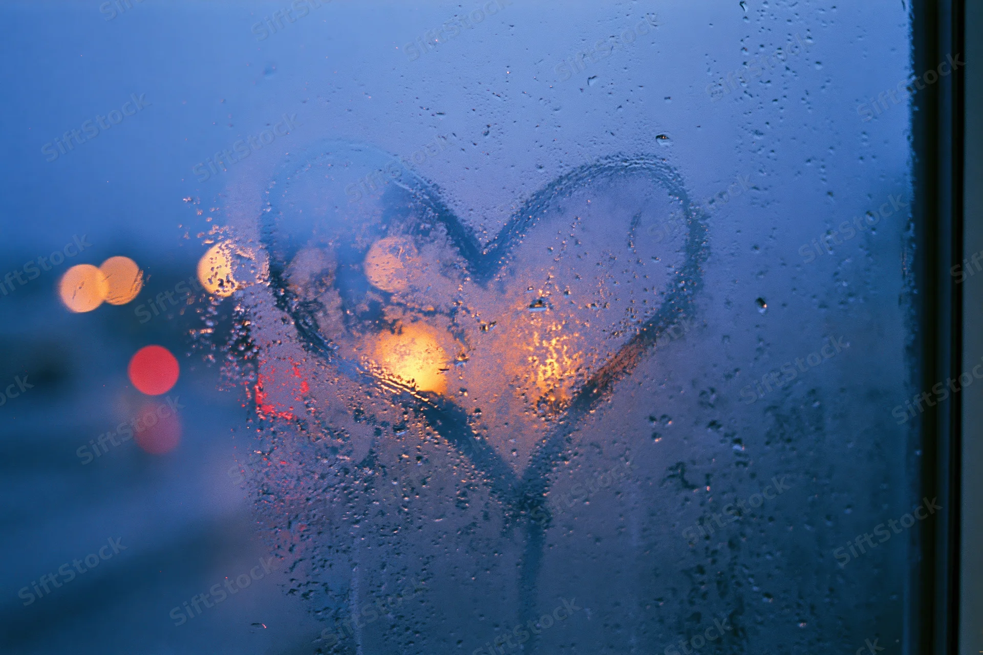 Heart drawn on fogged window with city lights glowing through at twilight