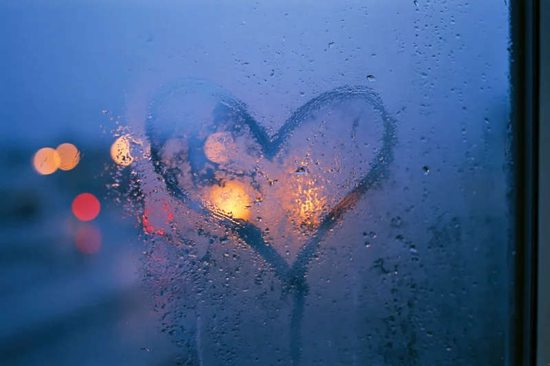 Heart drawn on fogged window with city lights glowing through at twilight