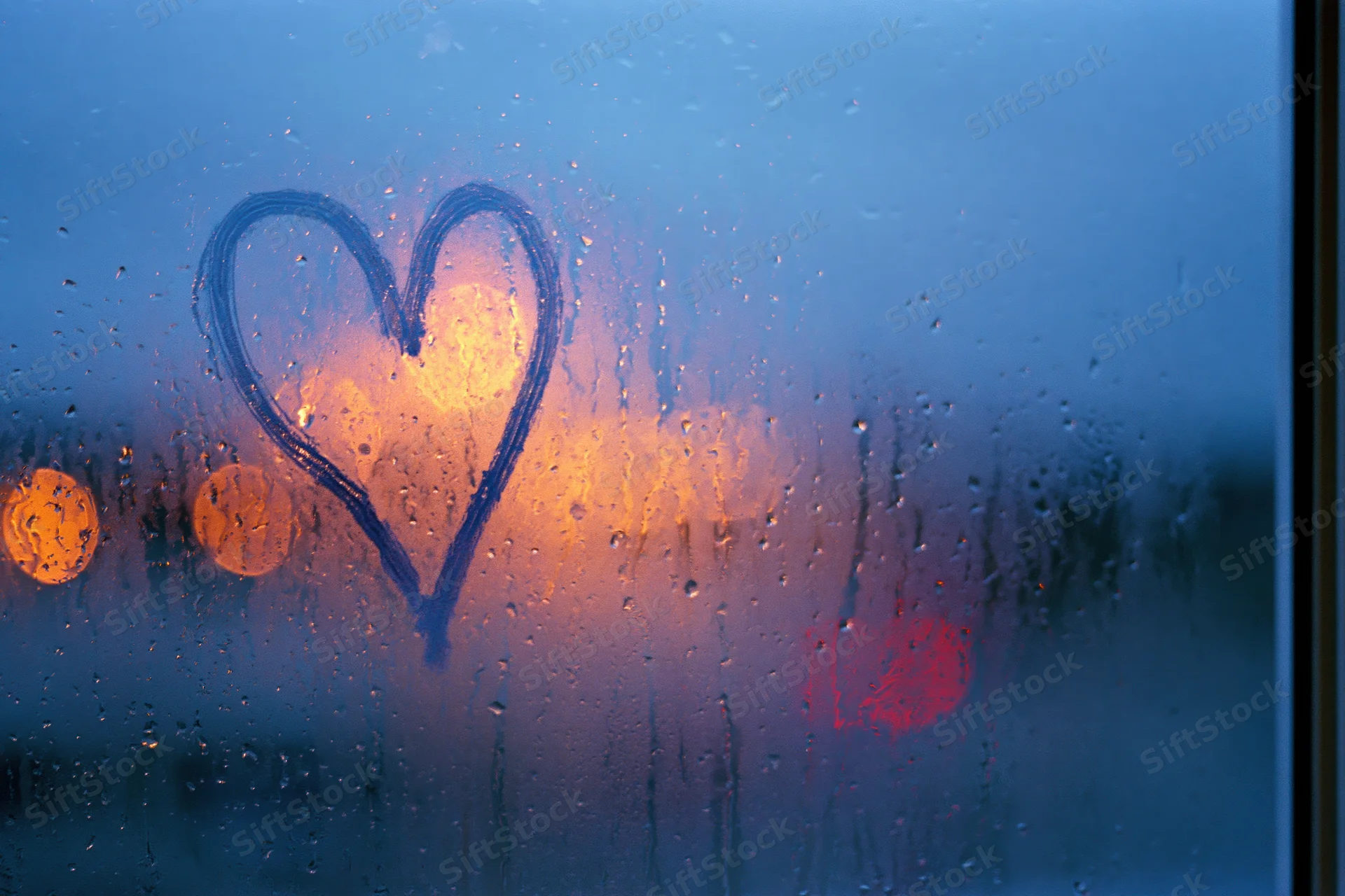 Heart drawn on fogged window with raindrops and blurred city lights at twilight