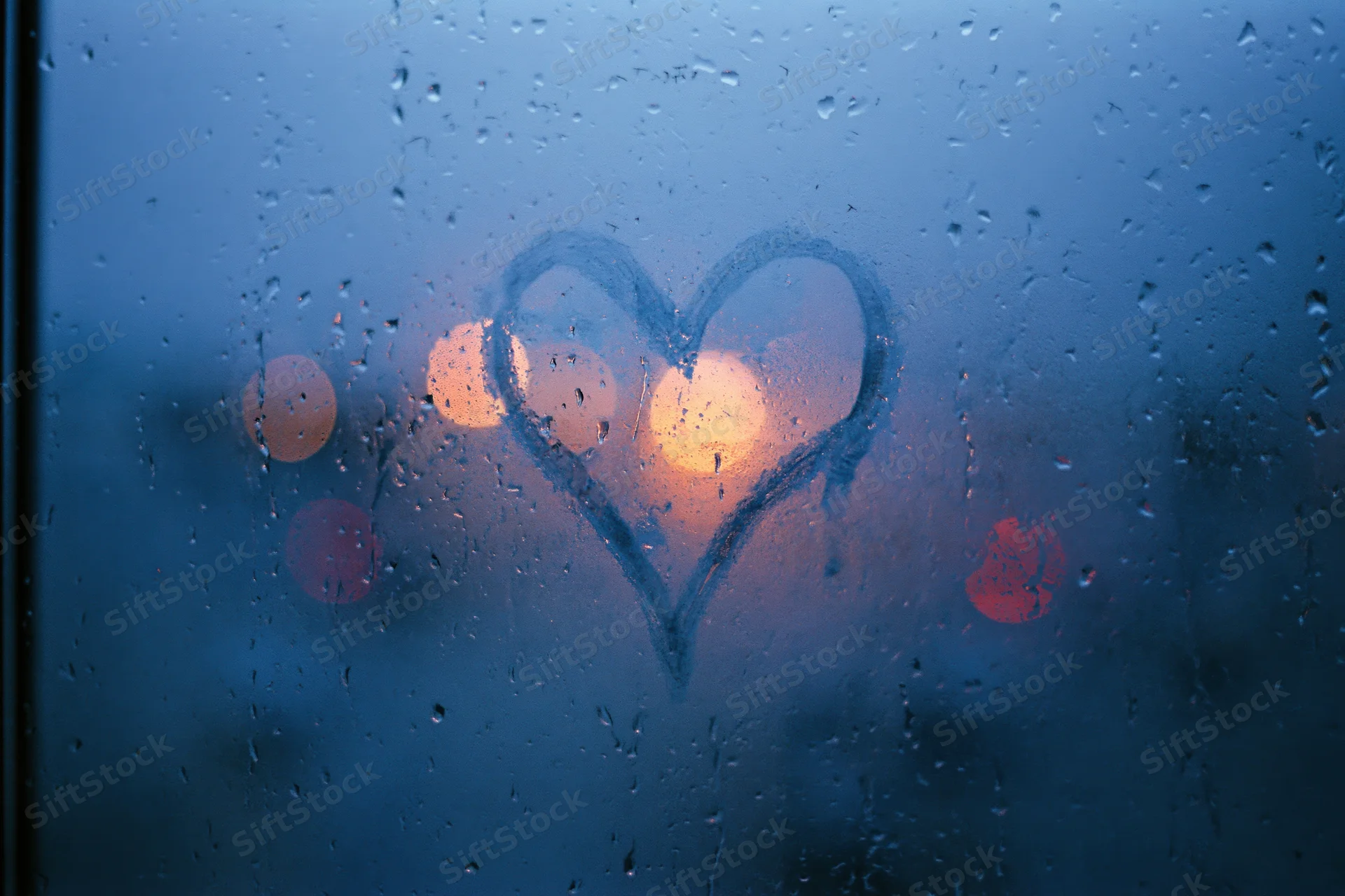 Heart drawn on fogged rain-covered window with blurred city lights behind