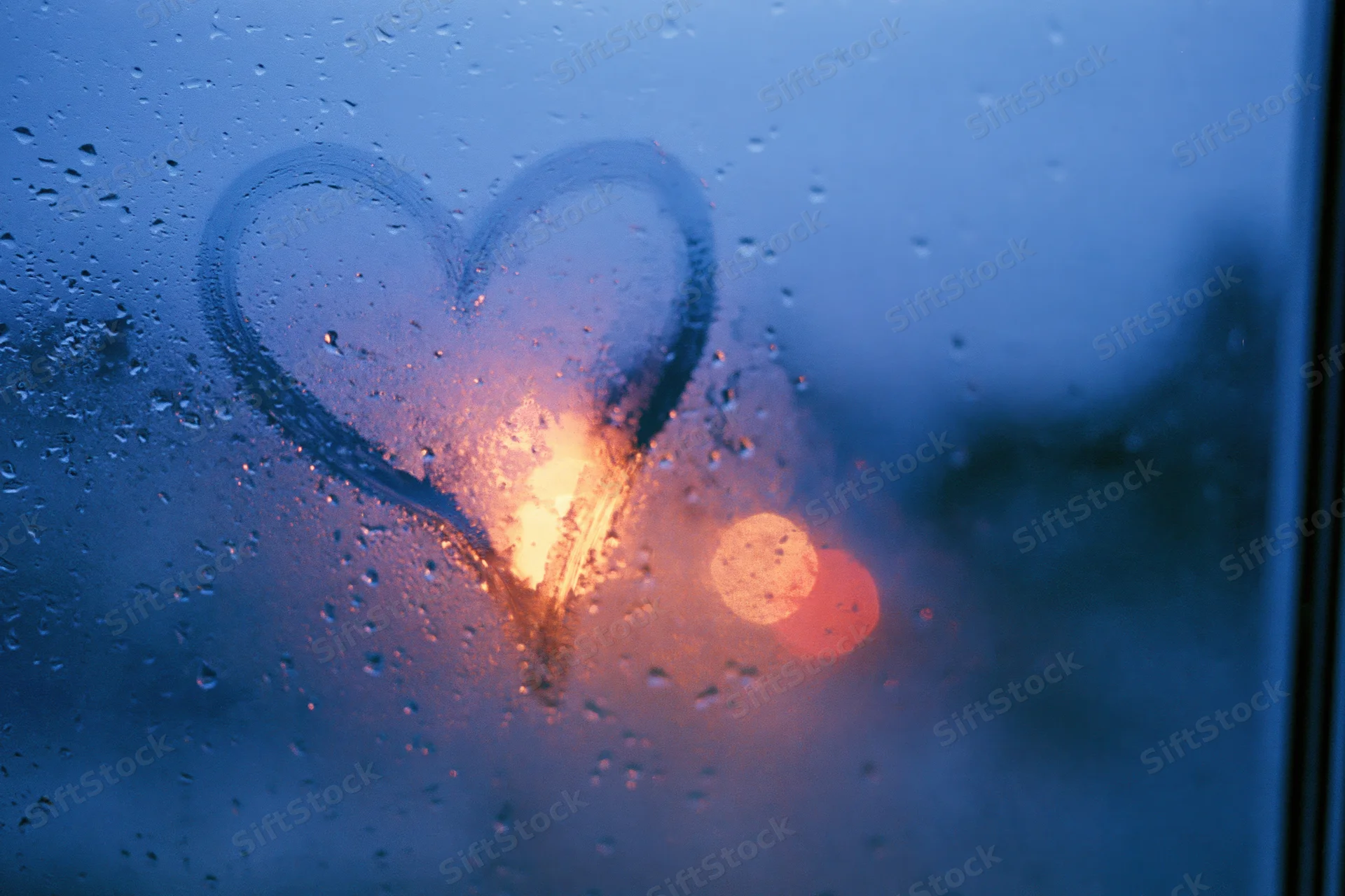 Heart drawn on fogged window with raindrops and blurred city lights visible through it