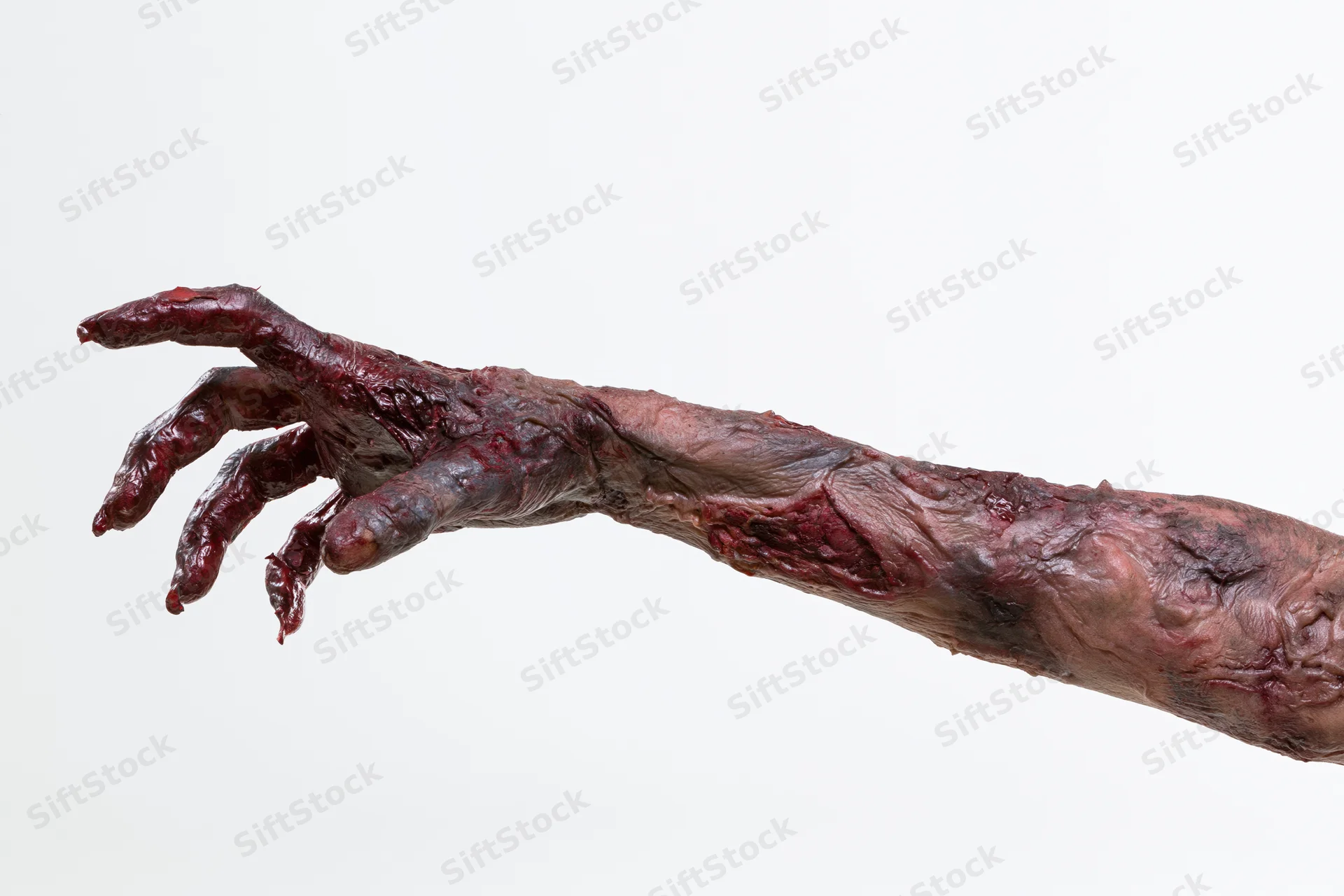 Zombie hand with prosthetic makeup and decayed skin reaching out against white background
