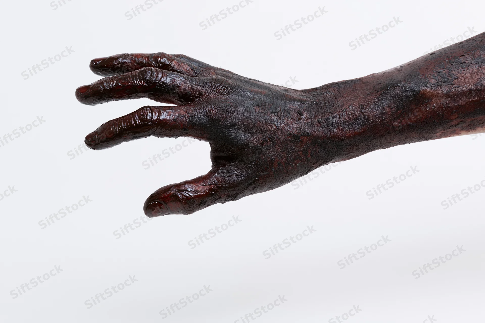 Closeup of a dark-skinned hand and forearm covered in thick black oil, isolated on white background