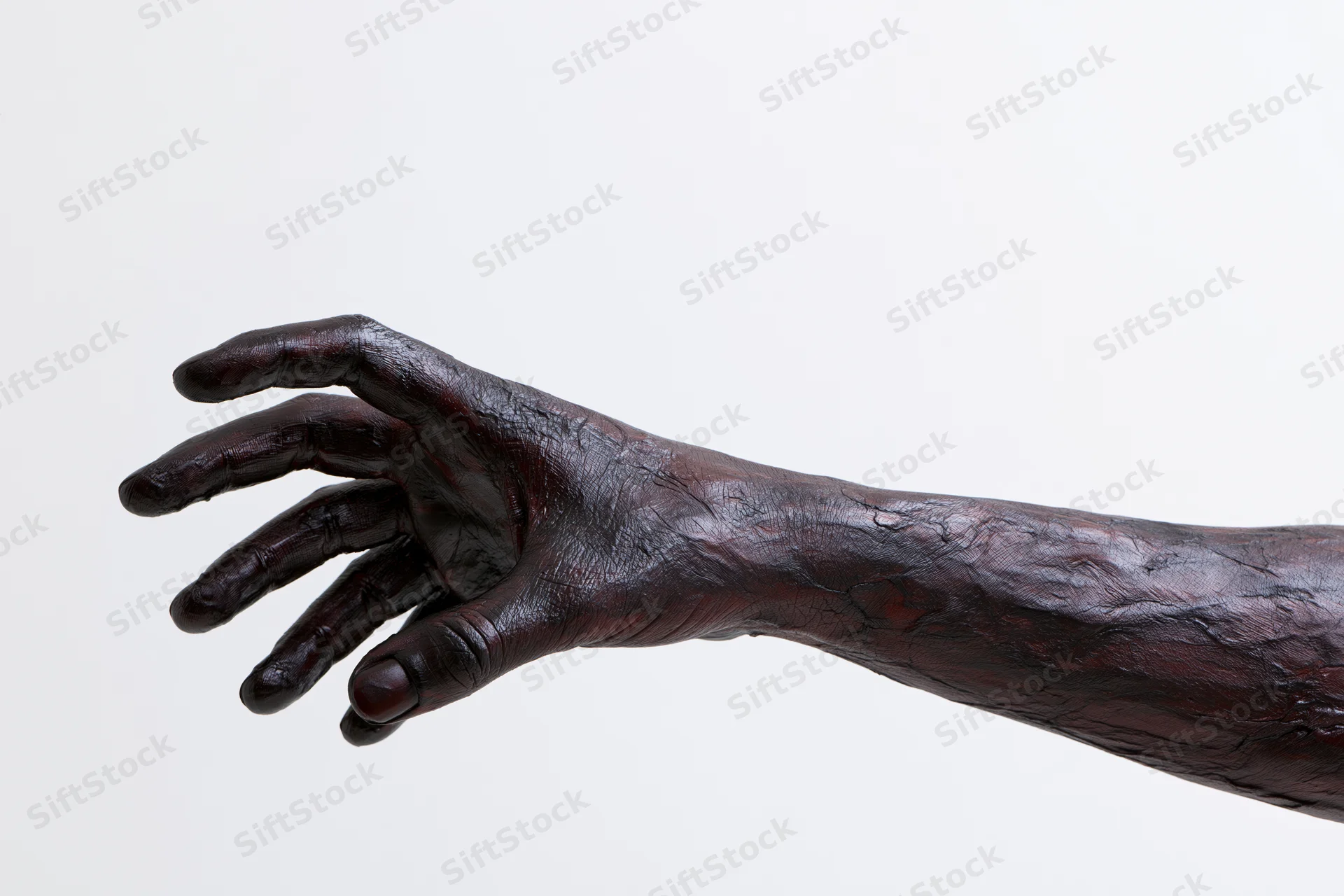 Bronze sculpture of a human hand and forearm with textured dark surface extending against white background