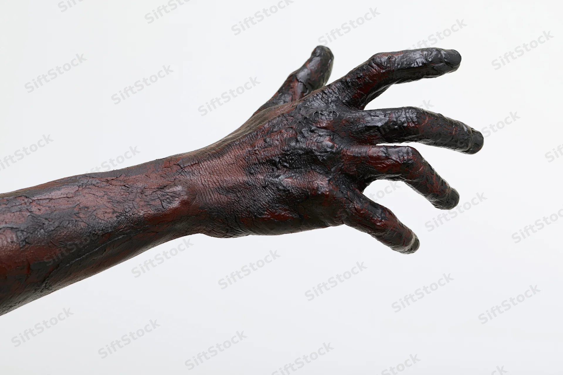 Blackened hand and forearm extended against white background, covered in thick dark oil or grease, showing textured skin and industrial residue