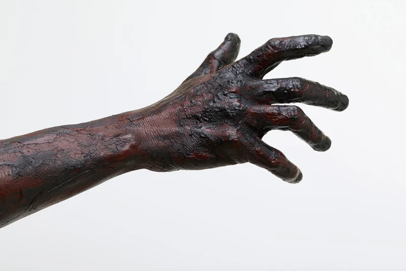 Blackened hand and forearm extended against white background, covered in thick dark oil or grease, showing textured skin and industrial residue
