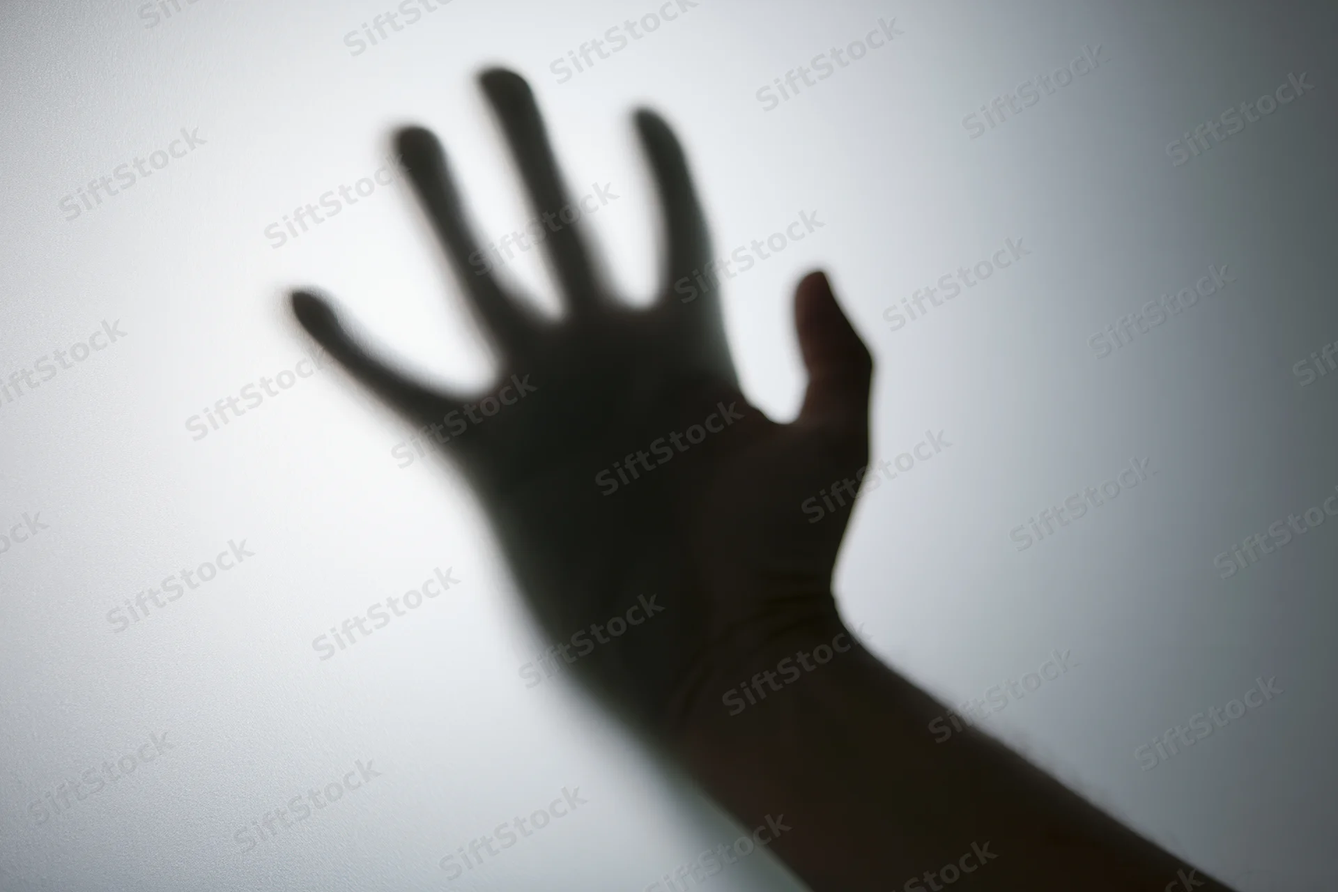 Shadow of a hand pressed against frosted glass with blurred edges and soft lighting