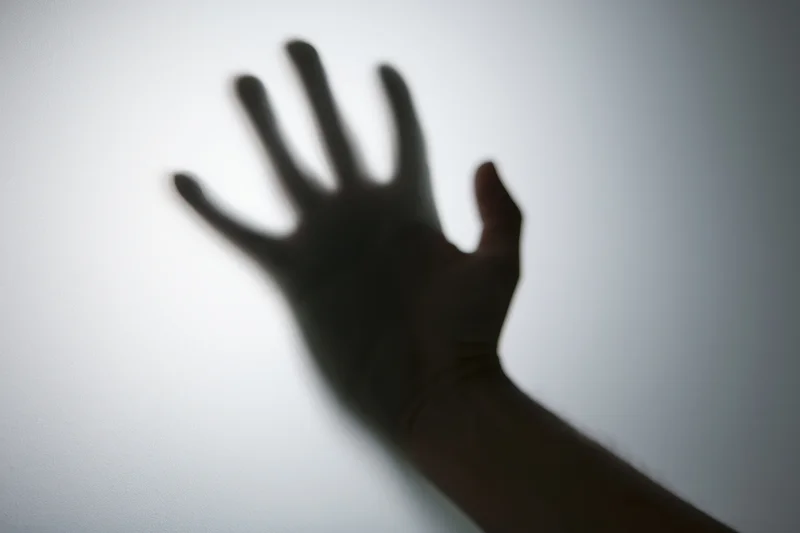 Shadow of a hand pressed against frosted glass with blurred edges and soft lighting
